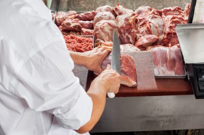 Cropped image of male butcher cutting meat at display cabinet in butchery